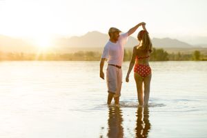 Couple dancing in lake water during golden hour with mountains in background.