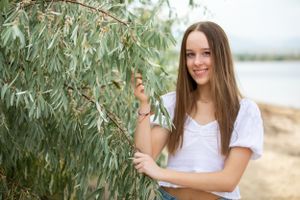 Person in white t-shirt standing near willow tree branches by waterfront.