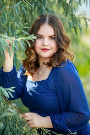 Portrait of person in navy blue top posing with willow branches outdoors.