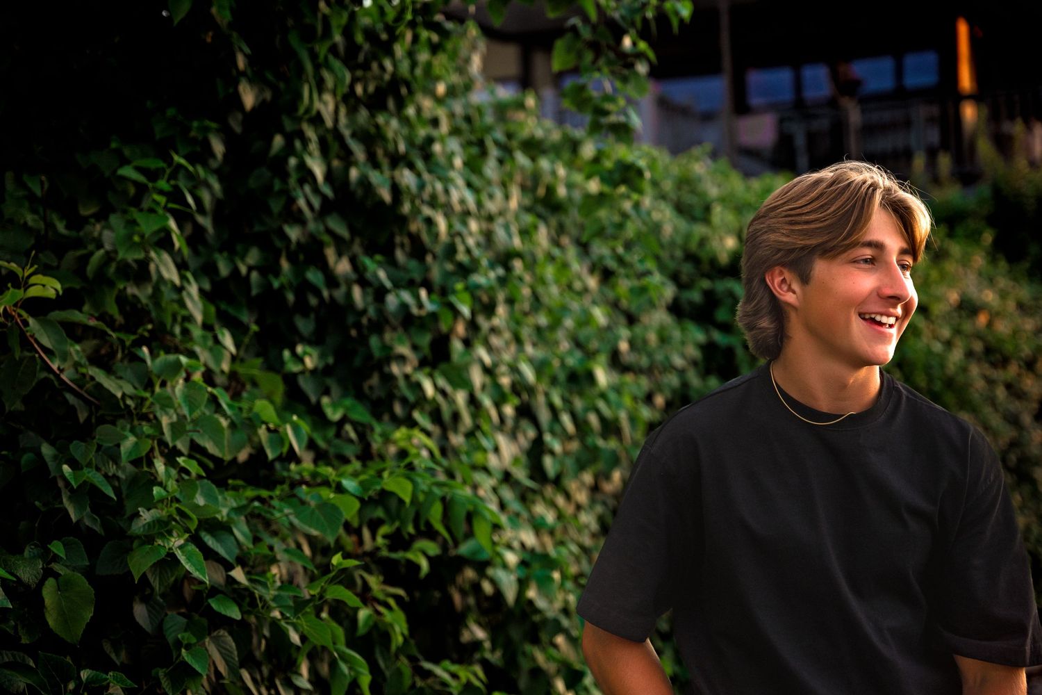 high school senior boy standing against greenery wall