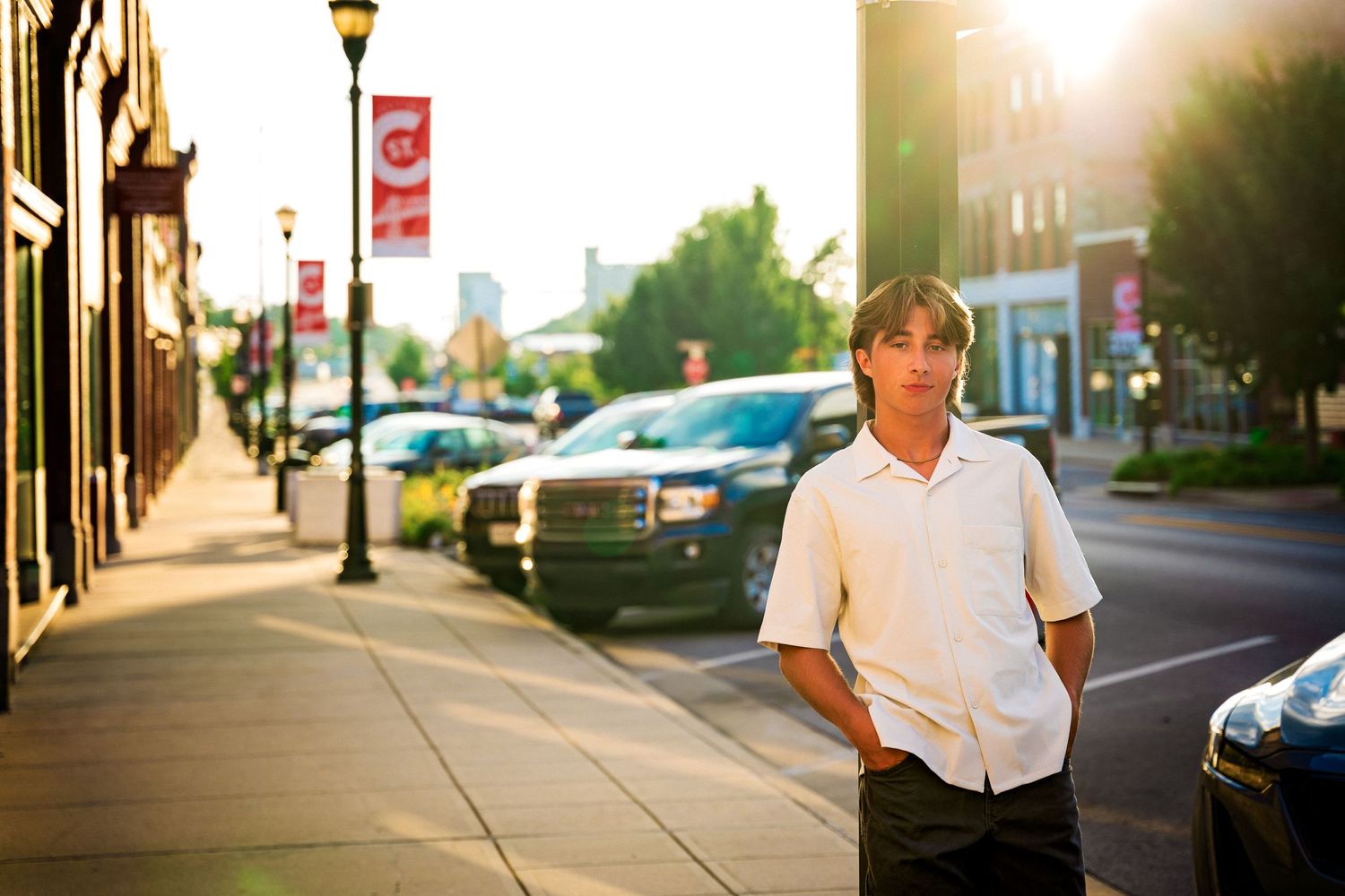 high school senior boy standing in front of light pole on commercial street
