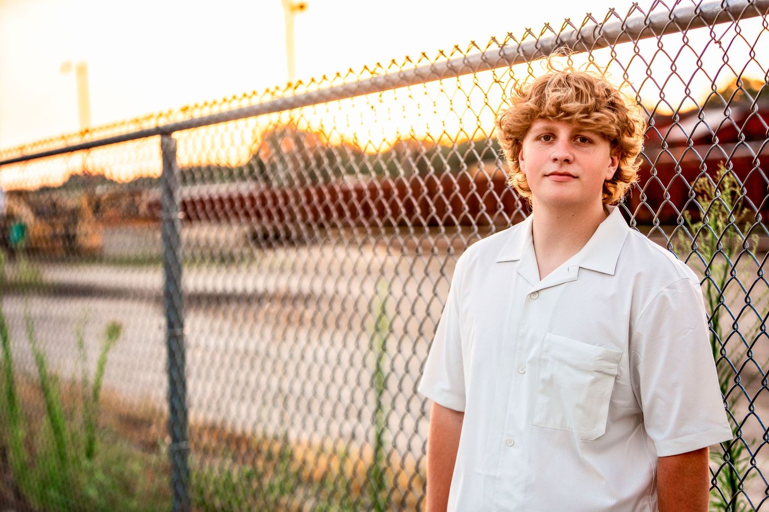 high school senior boy standing in front of fence on commercial street