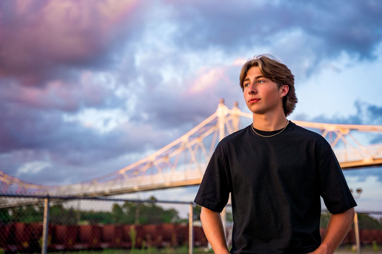 Senior boy portrait in front of bridge at sunset