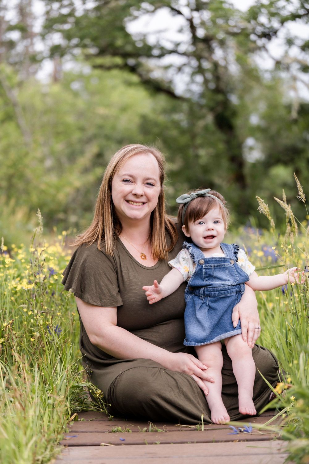 A caring moment outdoors on a wooden path surrounded by tall grass and wildflowers on a summer day. Family photography.