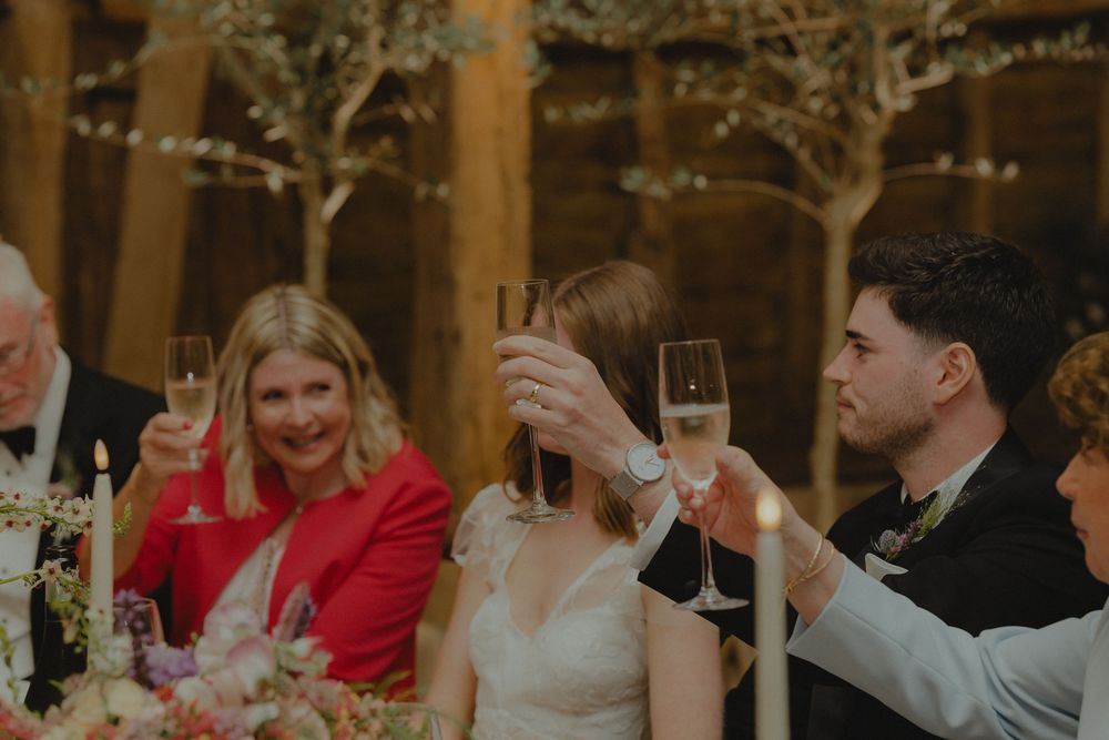 Bride and groom raise champagne glasses in a toast at elegant barn wedding reception.