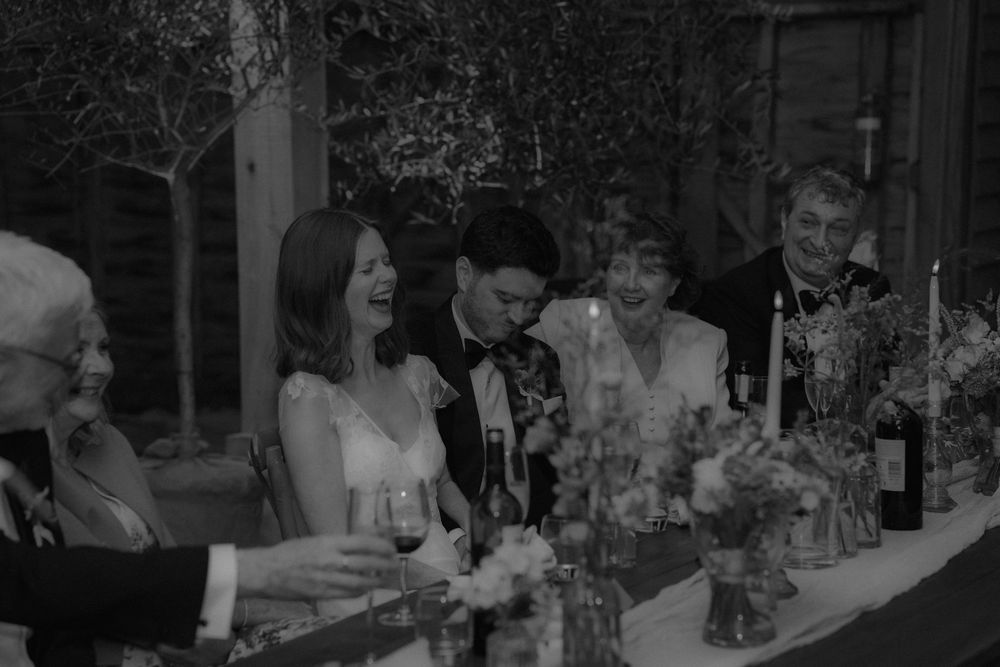 Bride and groom share joyful moment with guests at candlelit wedding reception table.