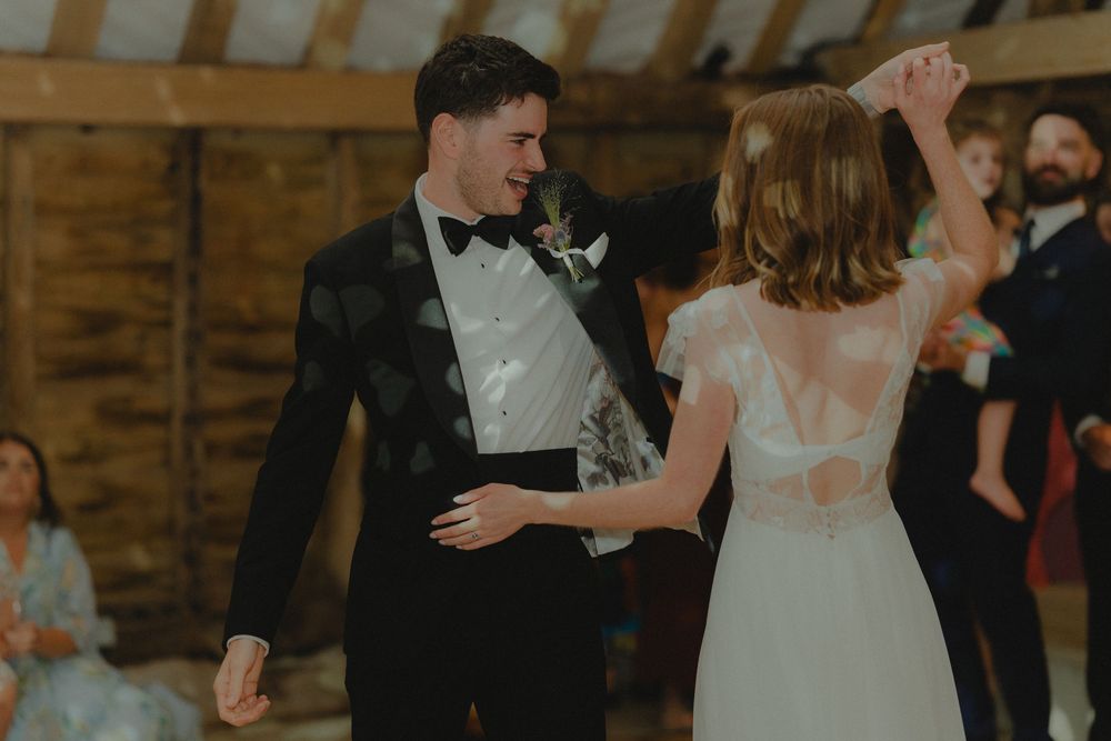 Bride and groom sharing their first dance in a rustic barn wedding venue, groom in black tuxedo.