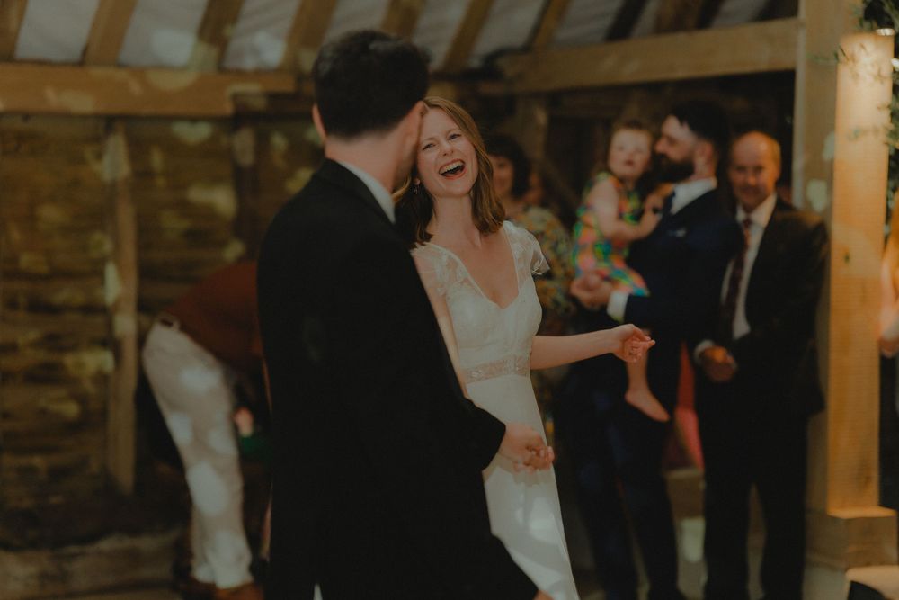 Bride in white gown laughing joyfully with groom during first dance at barn wedding.