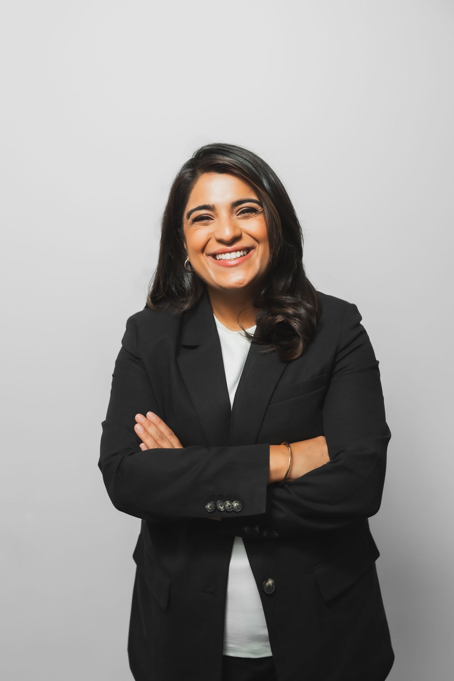 Professional woman in black blazer posing with crossed arms against grey background.