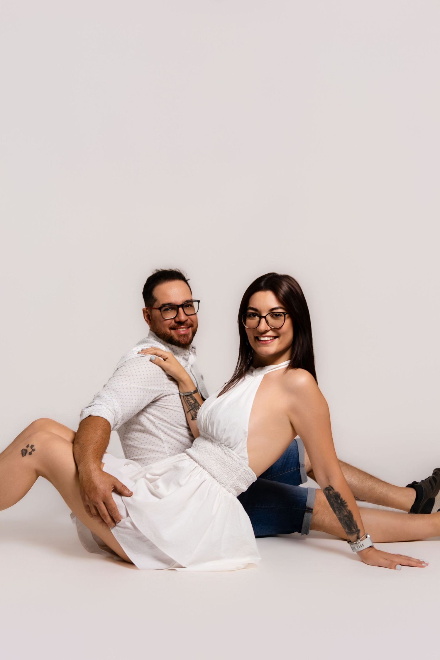 Casual couple in white and denim lounges on floor during studio photoshoot.