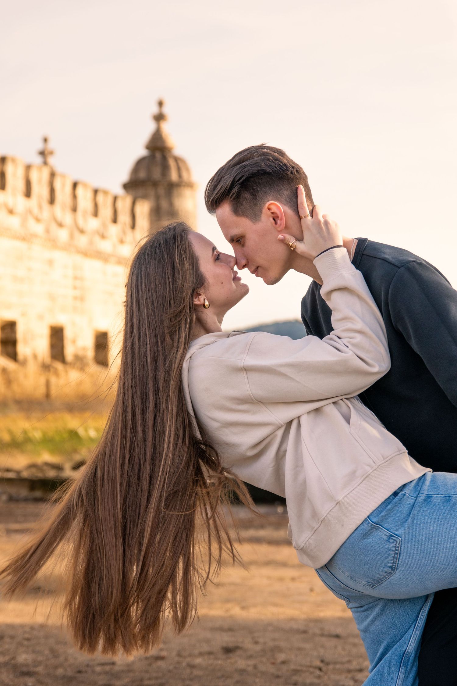 Romantic couple embracing at sunset with castle ruins in background.