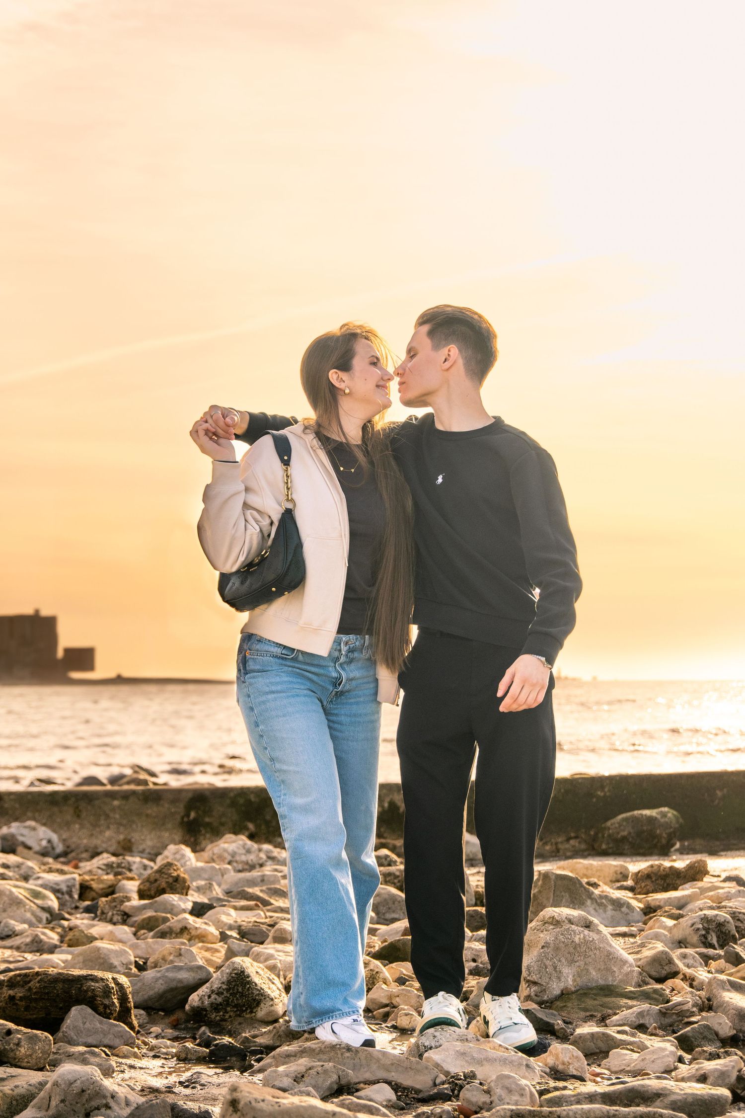 Couple sharing intimate moment on rocky beach during golden hour sunset.