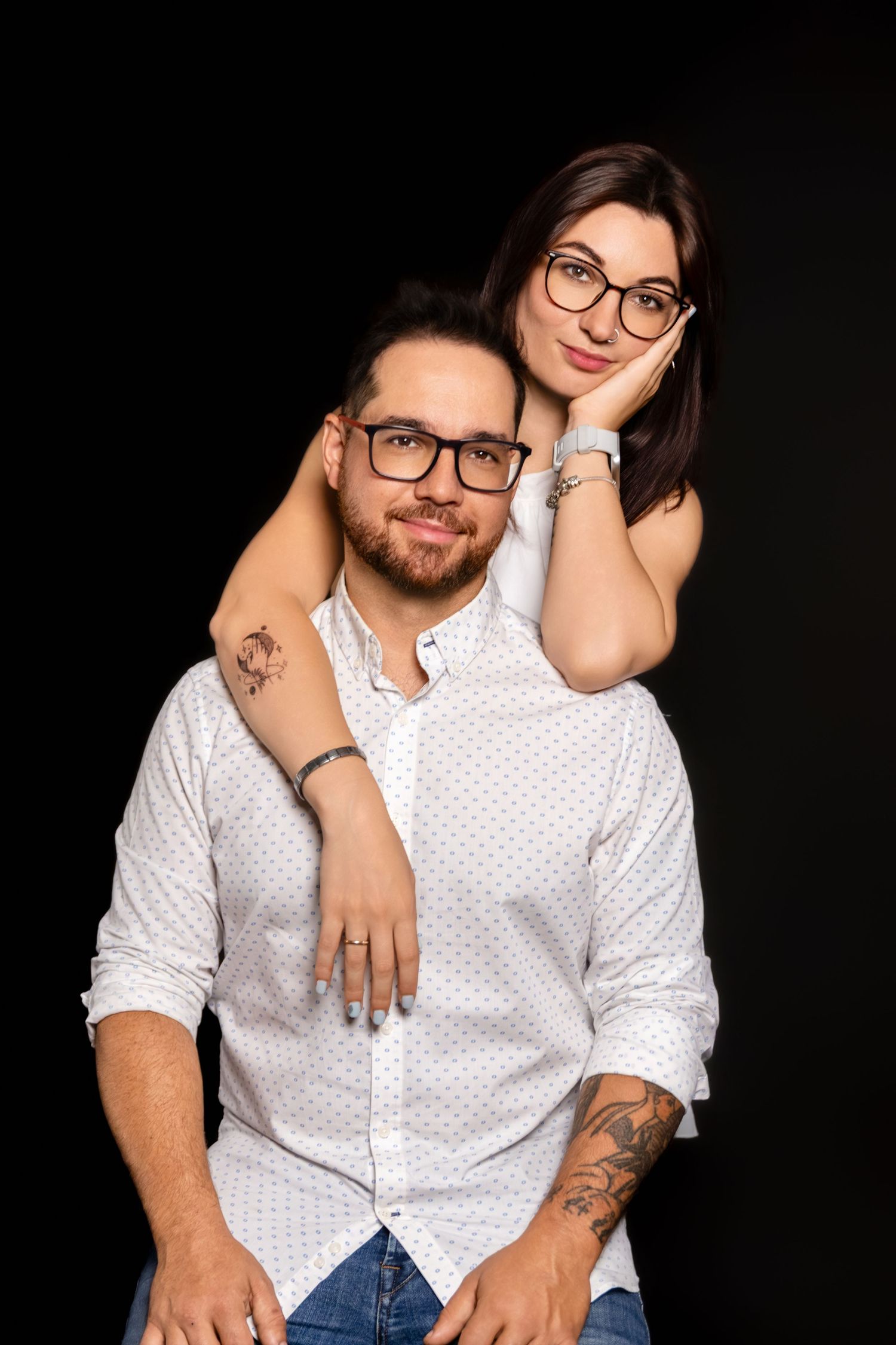 Couple in matching white shirts poses intimately against dark background.