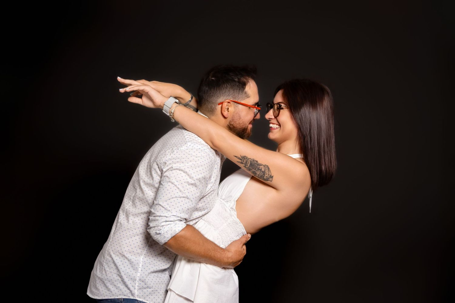 Couple in white outfits shares intimate dance pose against dark background.