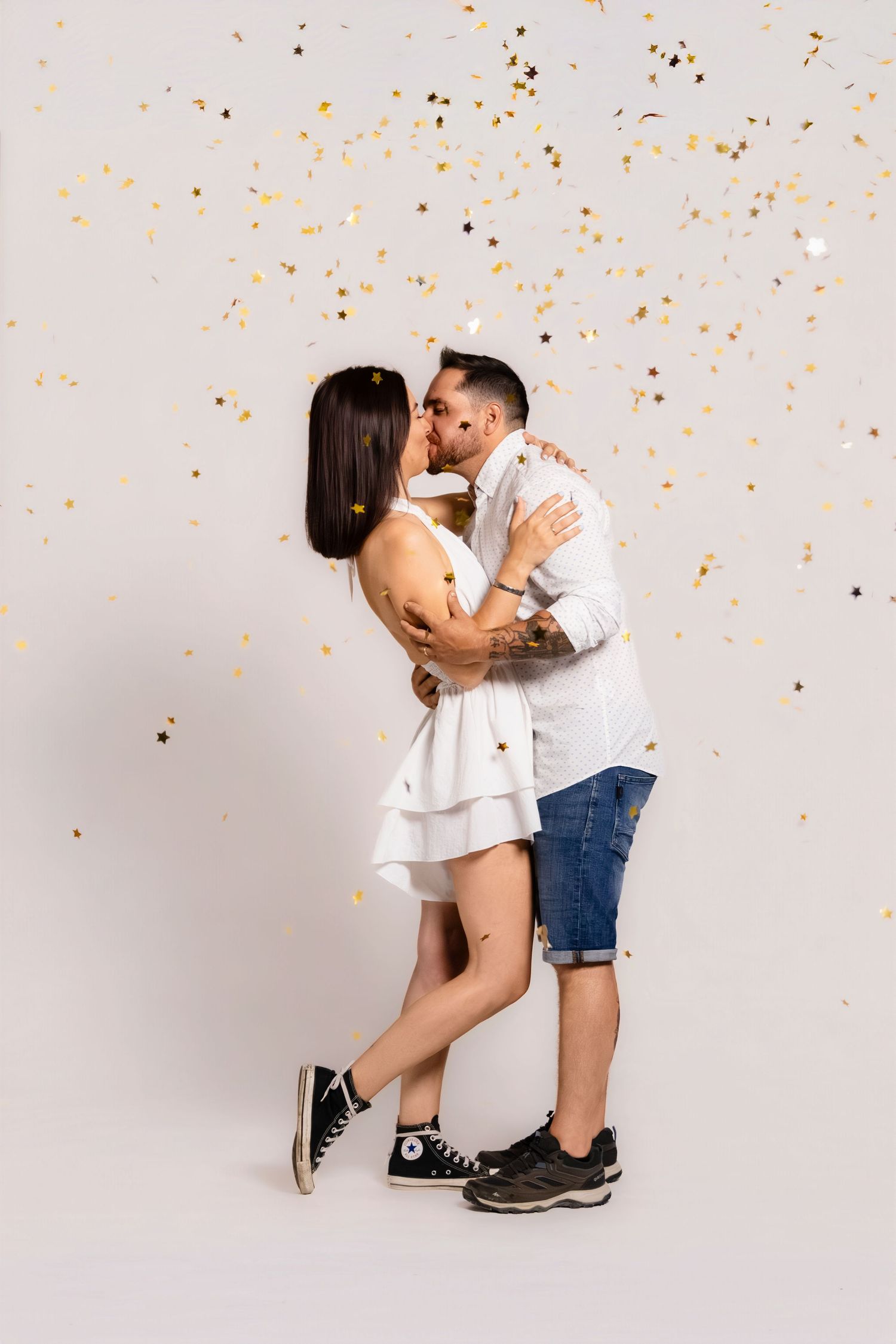Couple embraces under falling gold confetti against light background.