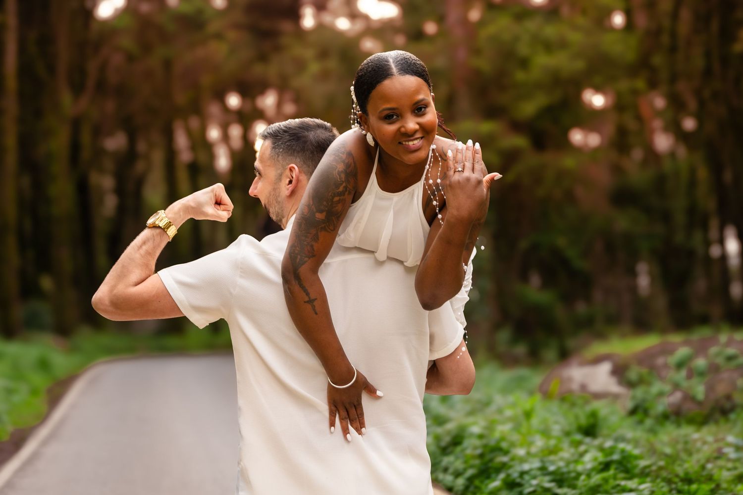 Two people in white outfits share joyful moments on a forest path at sunset.