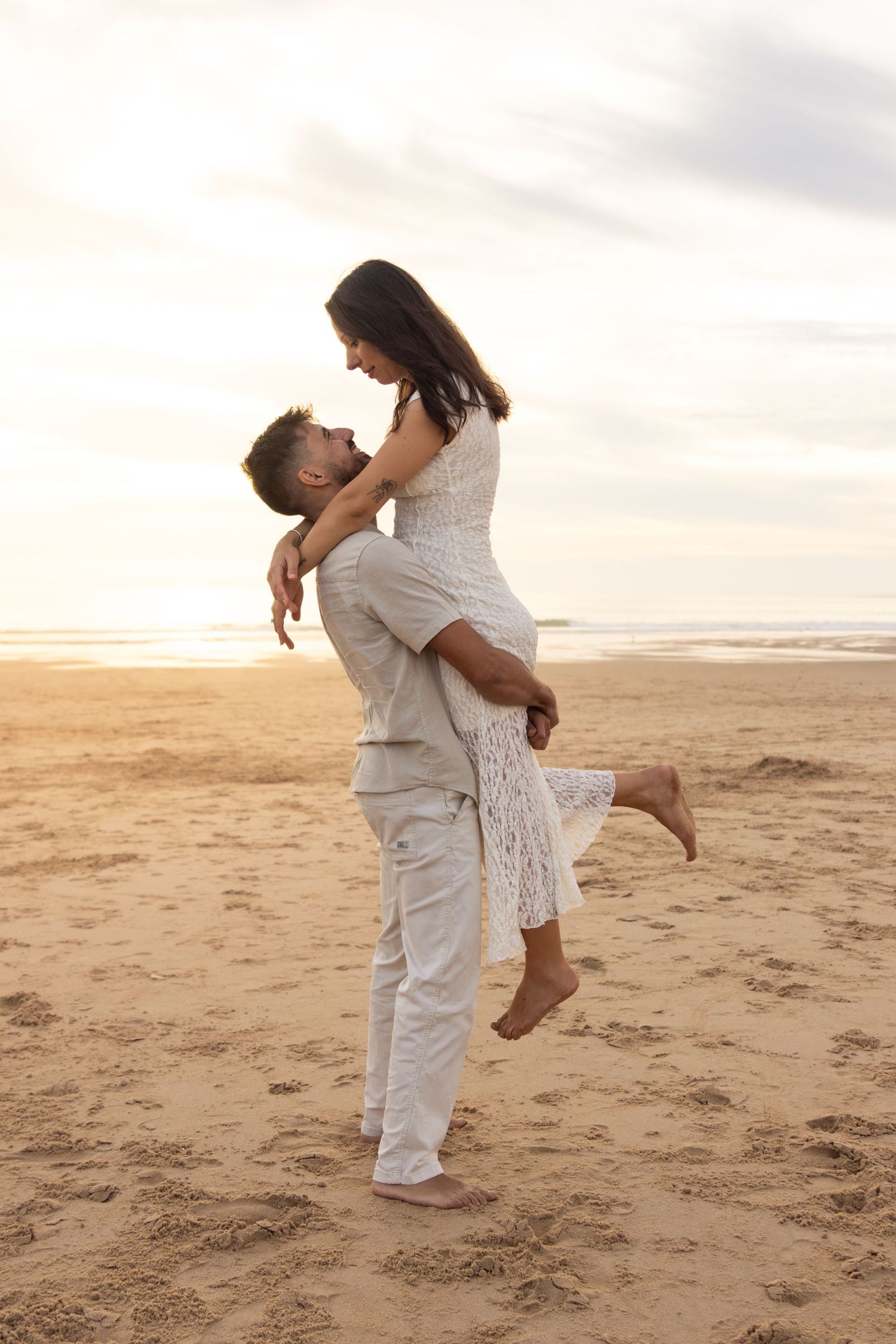Romantic couple in white clothing embracing and dancing on beach at sunset.