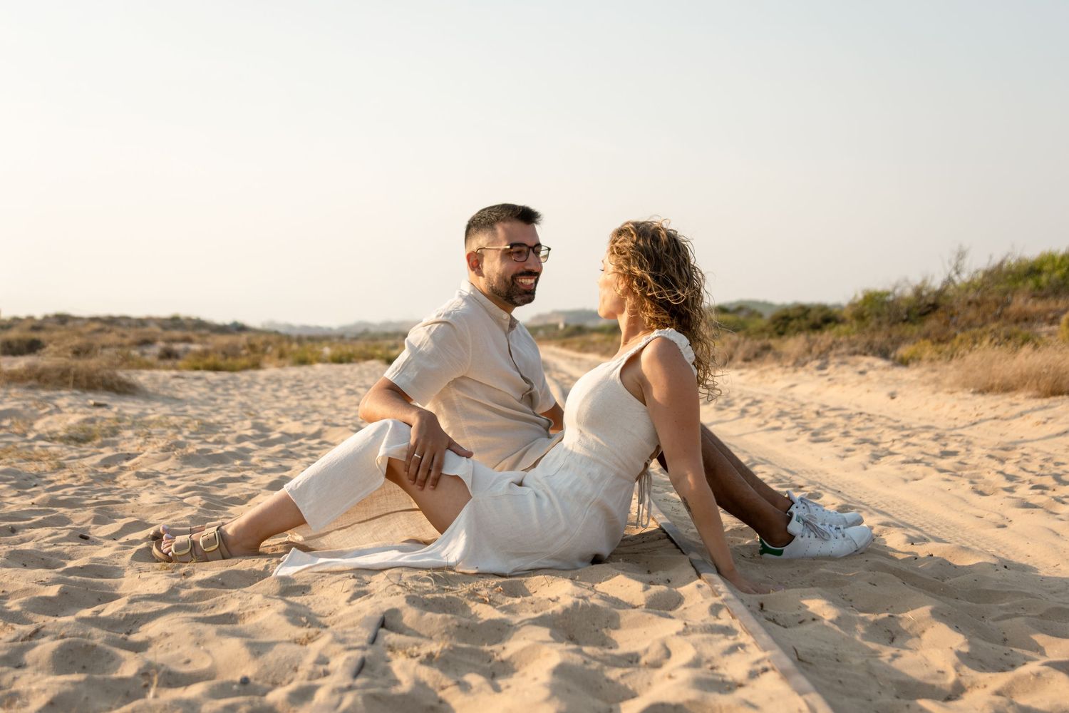 Couple relaxing together on sandy dunes during a beach photoshoot.