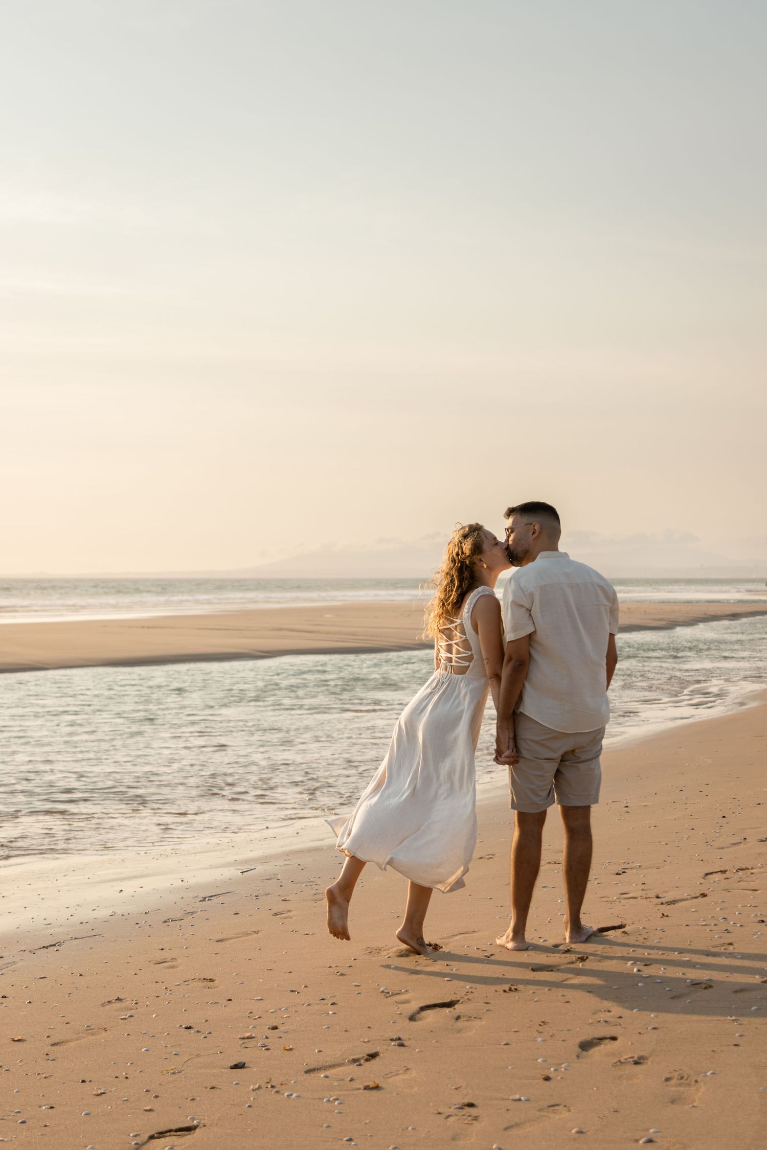 Couple walking hand in hand along a peaceful beach at sunset.
