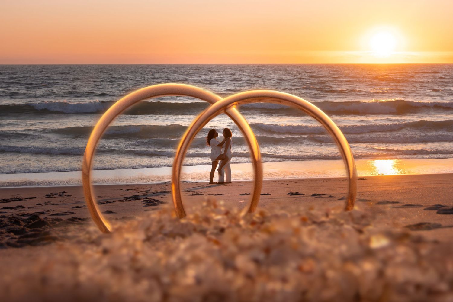 Wedding rings silhouetted against golden beach sunset with ocean waves.