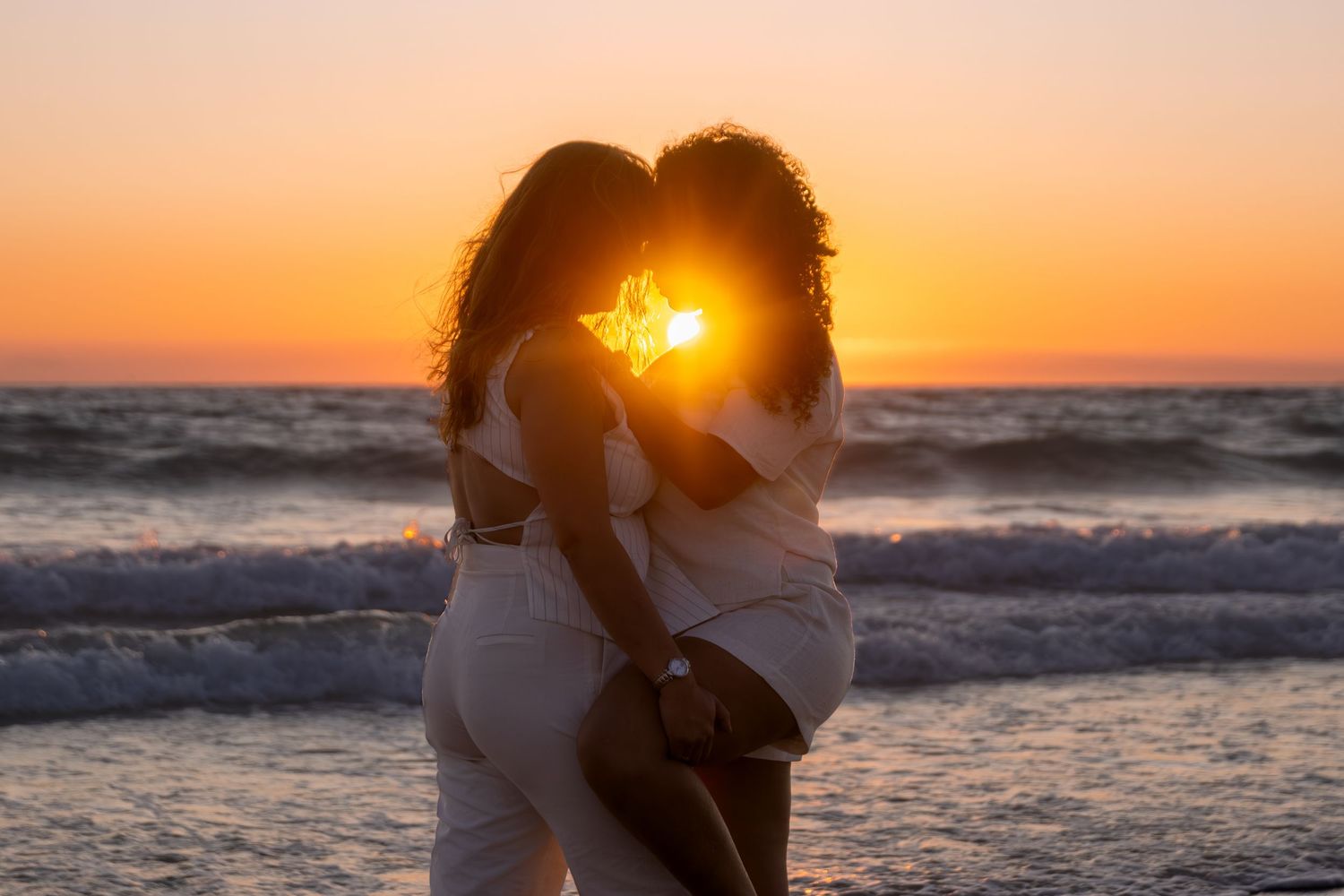 Silhouettes against dramatic orange sunset sky at beach.
