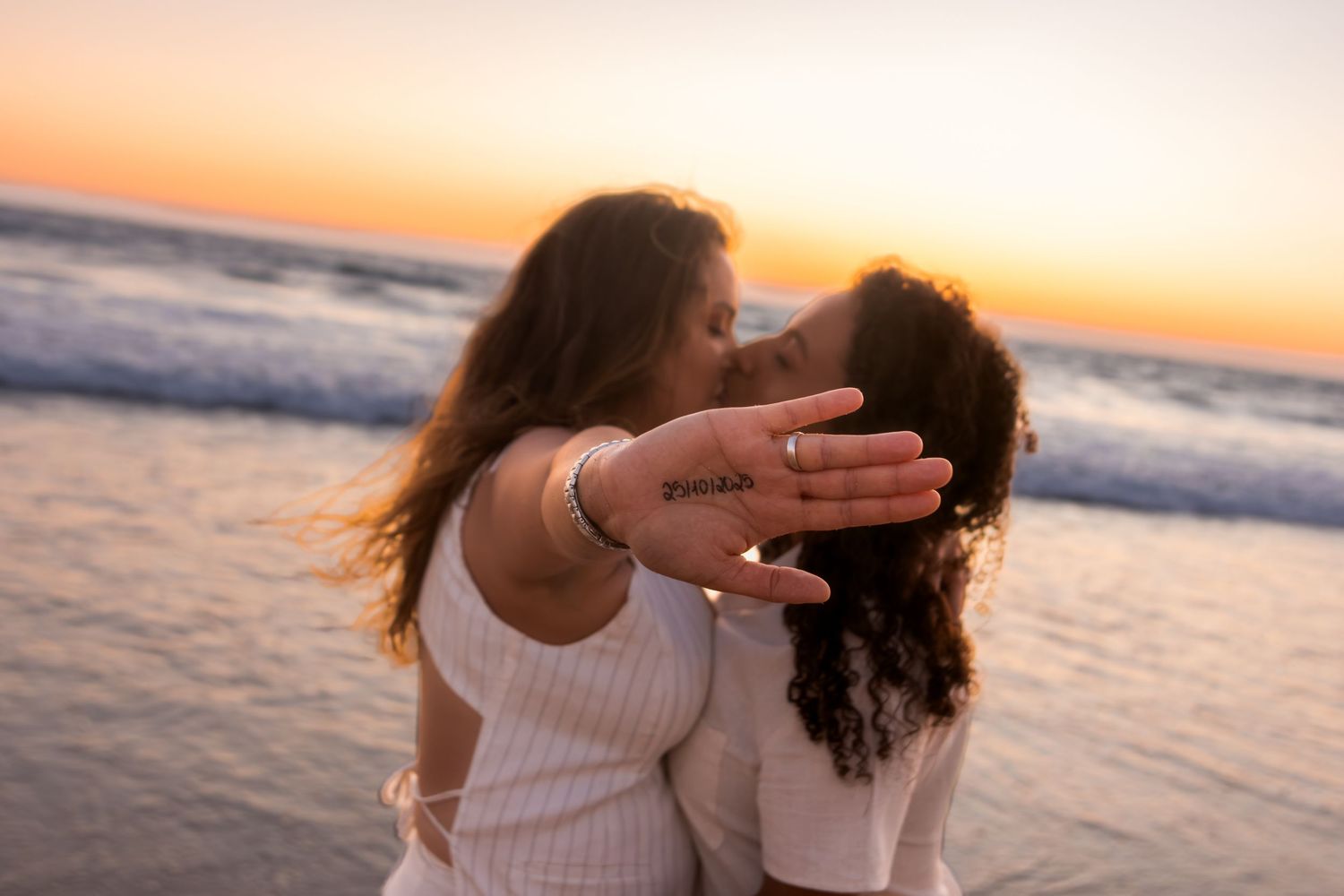 Couple embracing on sandy beach during golden hour with ocean waves in background.
