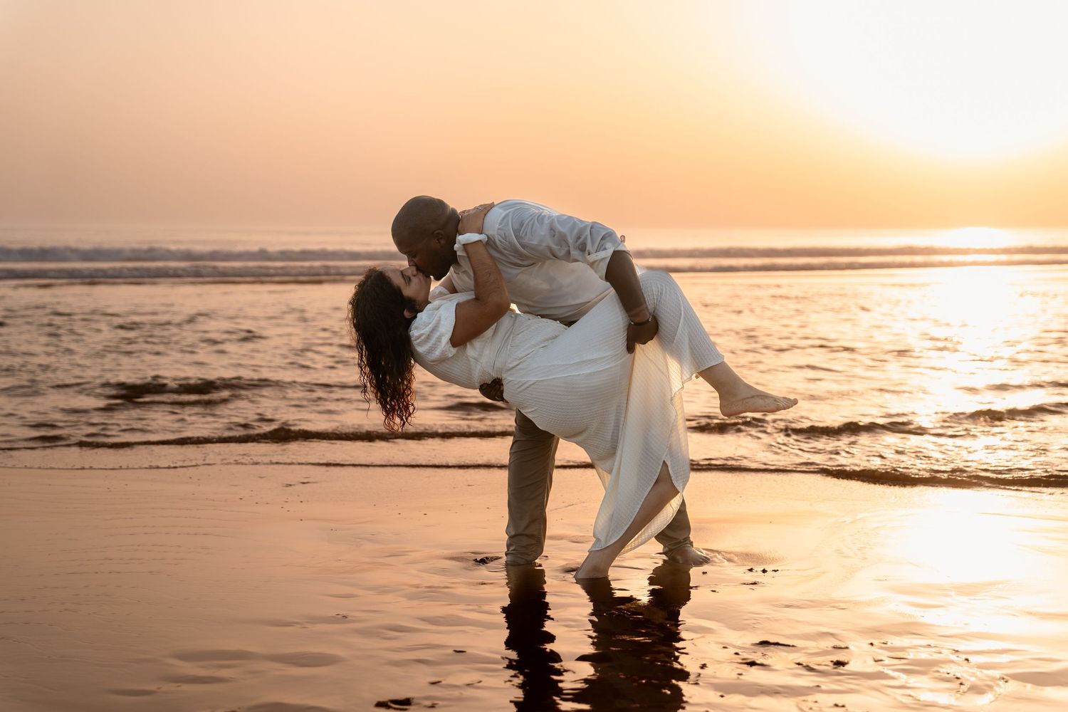 Romantic couple sharing an intimate dance pose on a beach at sunset.