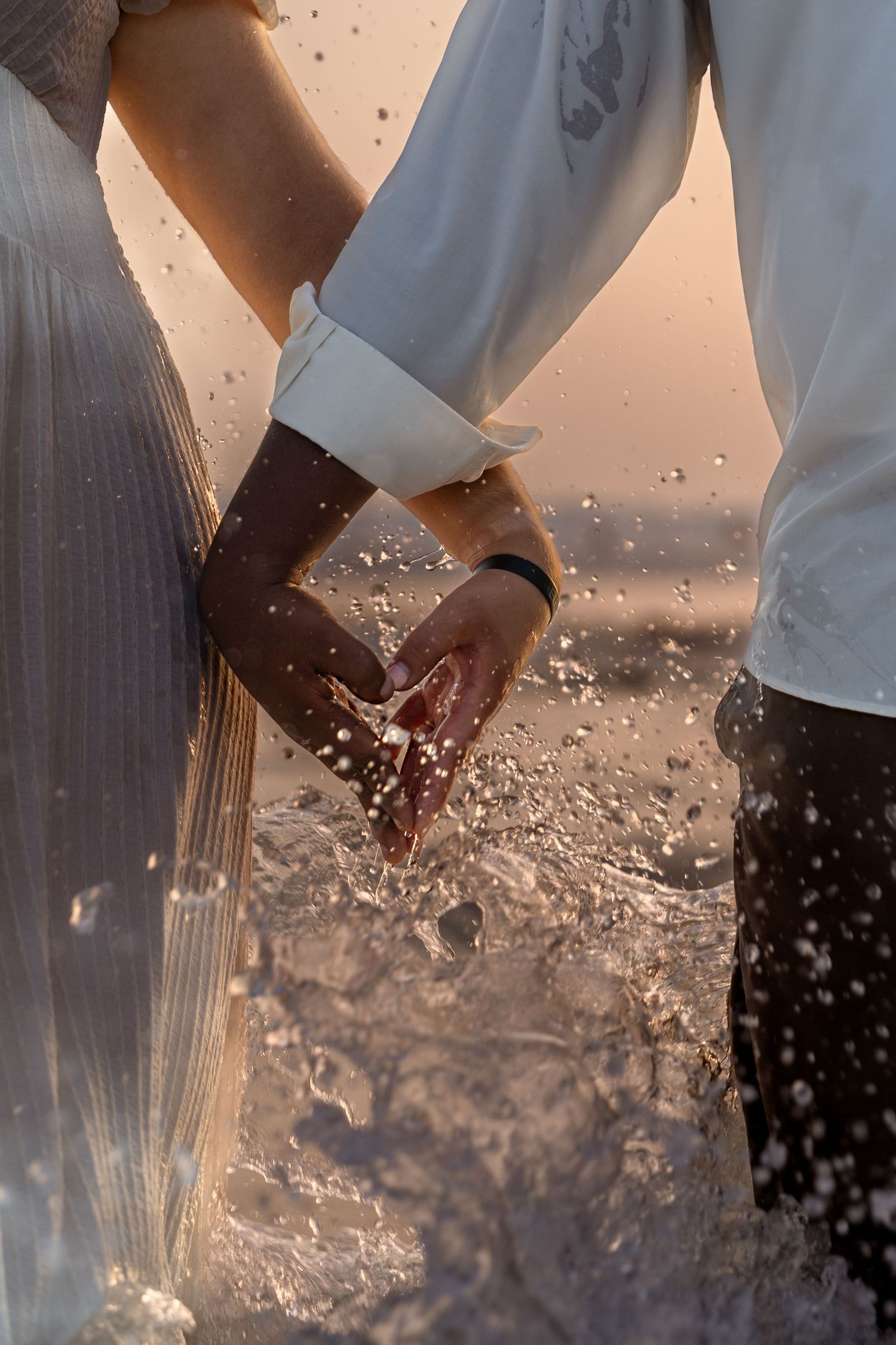 Clasped hands splashing in ocean water at golden hour.