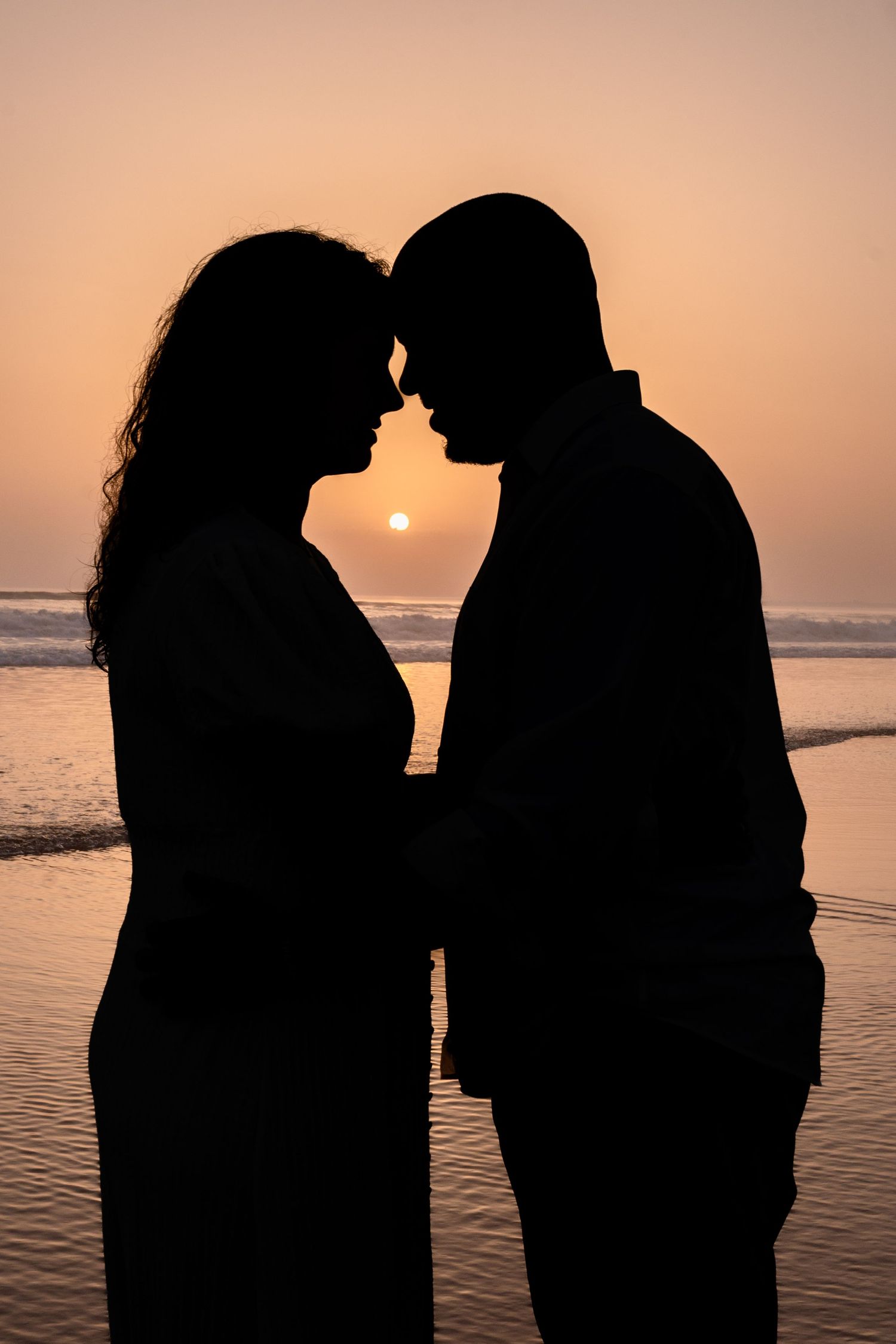 Silhouette of a couple facing each other against a sunset beach backdrop.