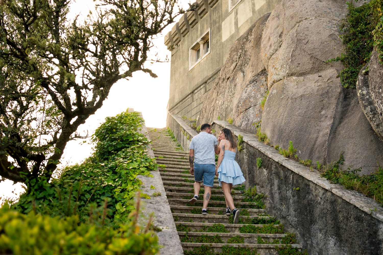 Stone steps wind up along an ancient fortress wall covered in vegetation.