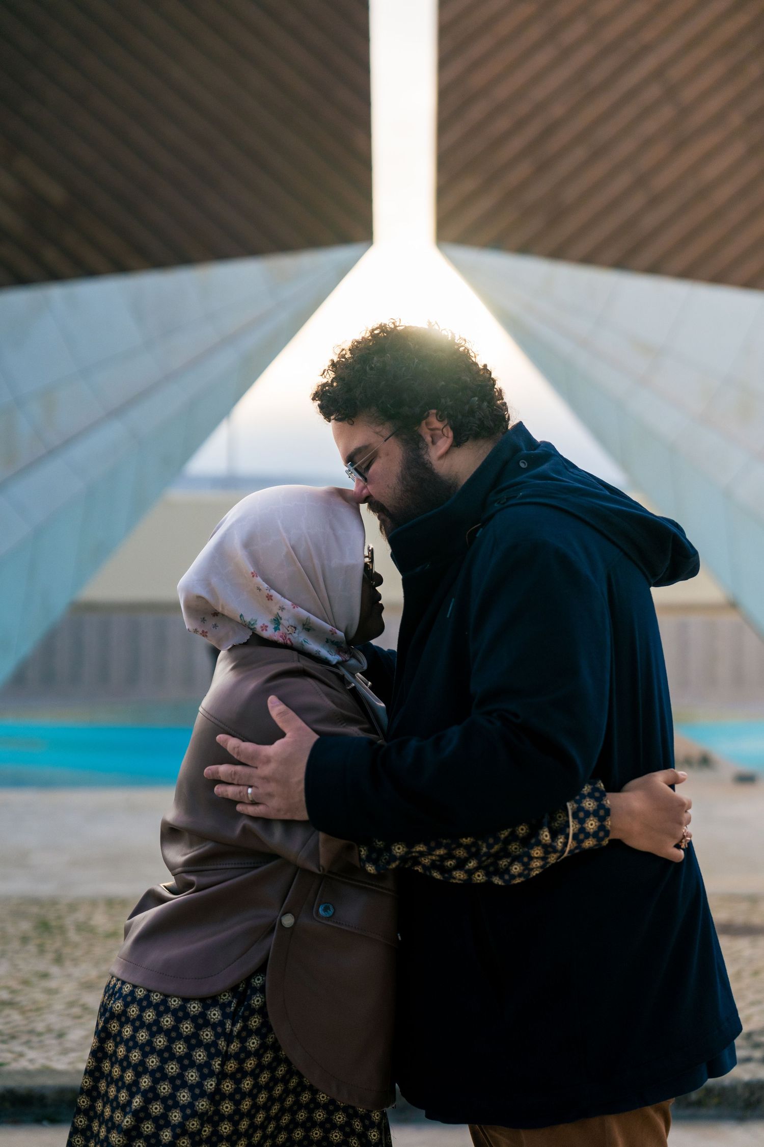 Intimate moment captured between two people embracing outdoors near modern architecture.