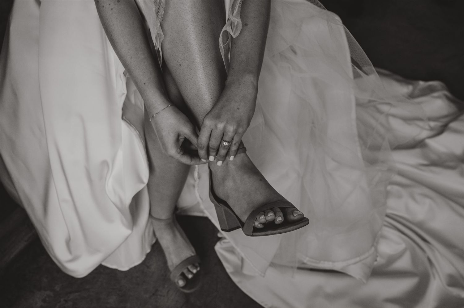 Black and white detail shot of bride adjusting her wedding shoes.