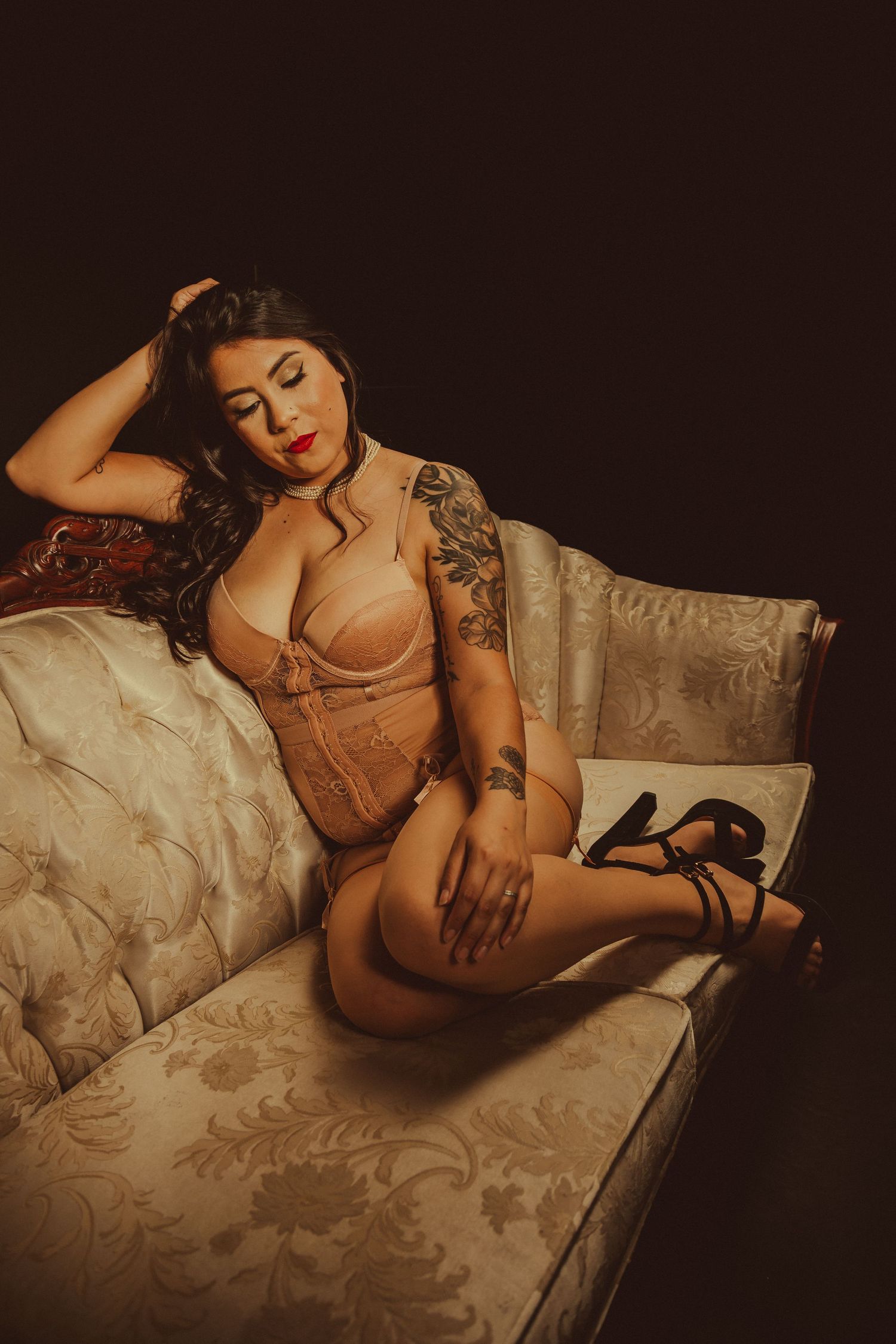 Artistic boudoir photo of person in lingerie posing on vintage couch.