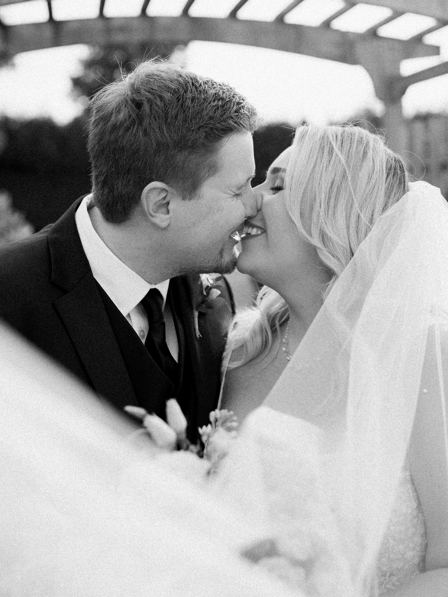 A close photo as a bride and groom lean in to a kiss, smiling brightly. Photo by Katie Crane Photography.
