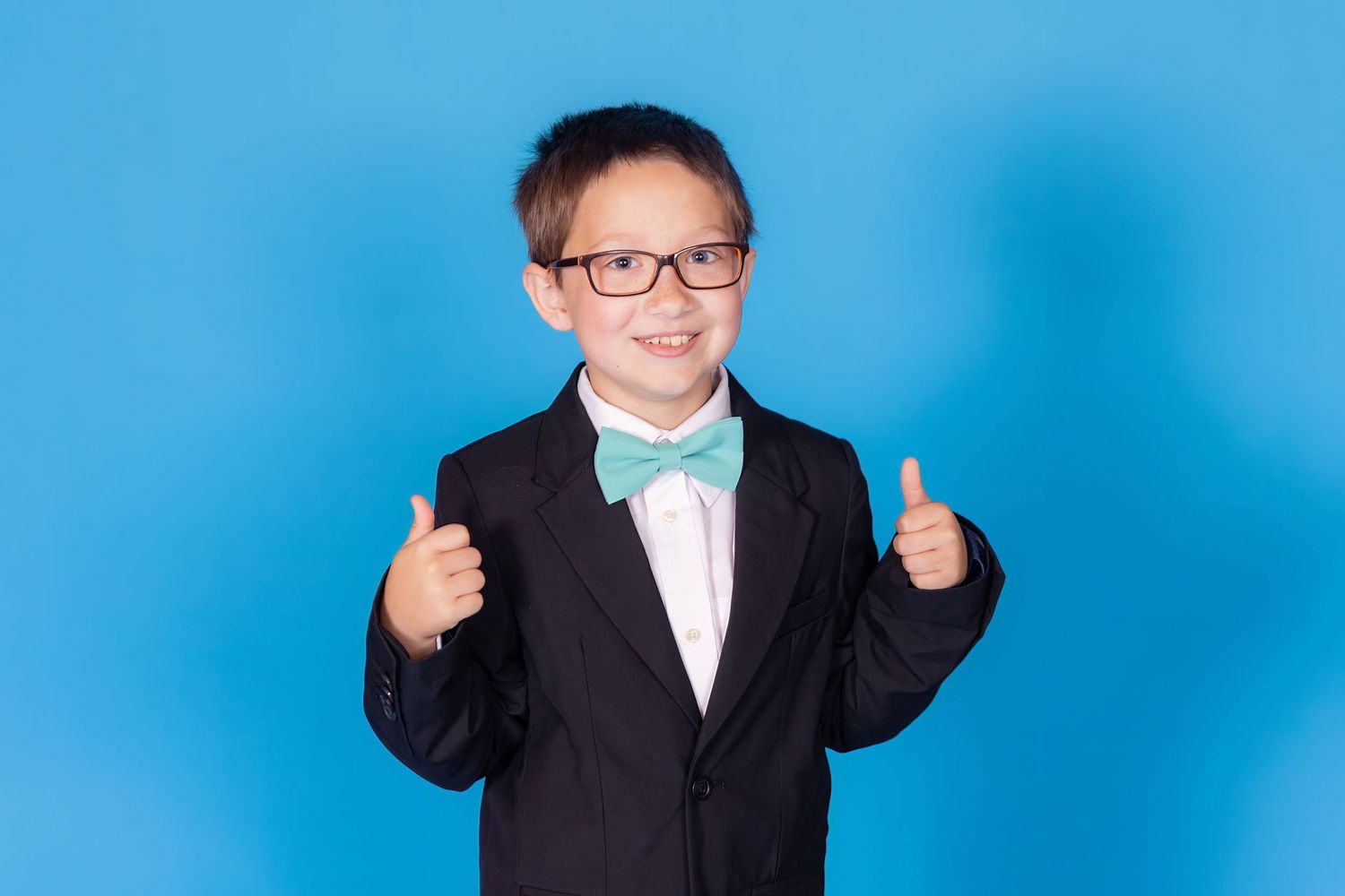 child in suit with bowtie on savage blue jay backdrop giving thumbs up in studio in clayton new jersey Gloucester county