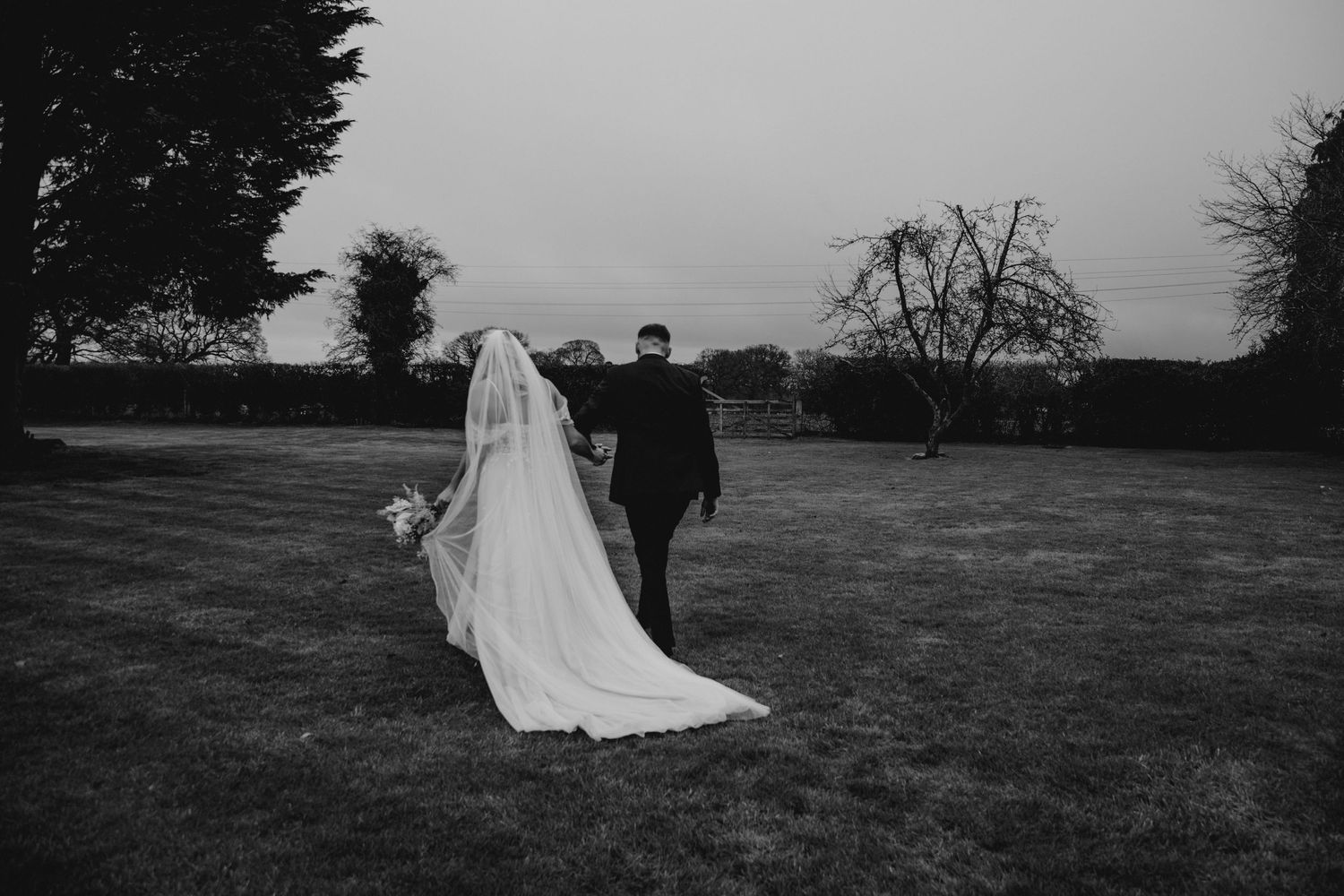 Black and white photo of newlyweds walking across an open field.