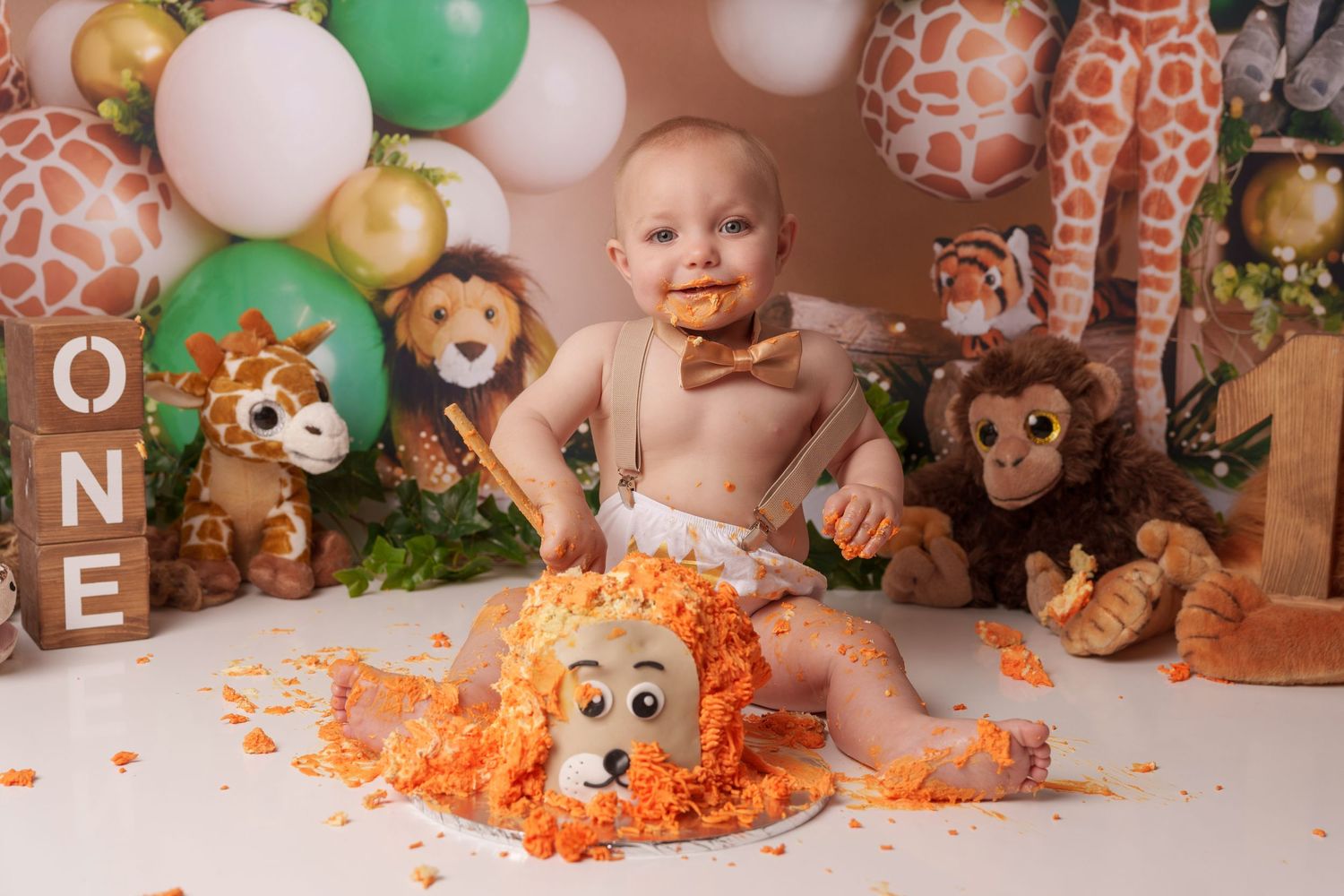 Safari-themed cake smash with stuffed animals and orange frosting mess on white backdrop.