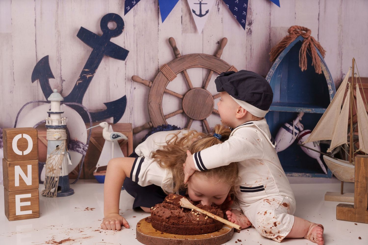 Nautical themed first birthday photo with sailor outfit and ship wheel decorations.