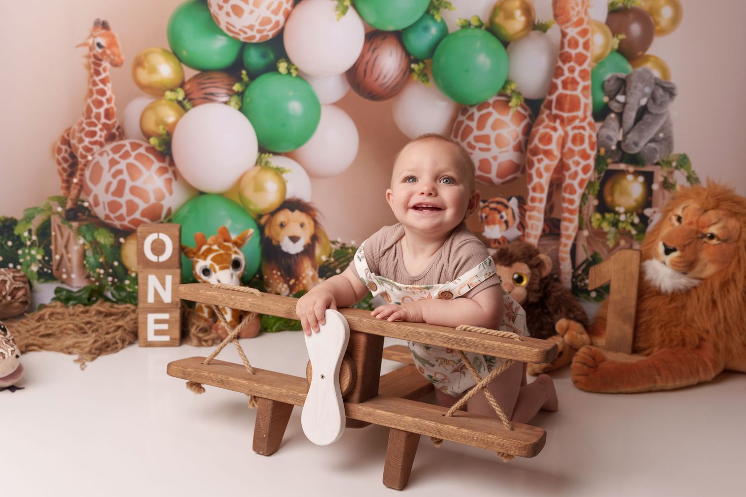 Safari-themed first birthday setup with wooden airplane prop, giraffes and balloon arch.