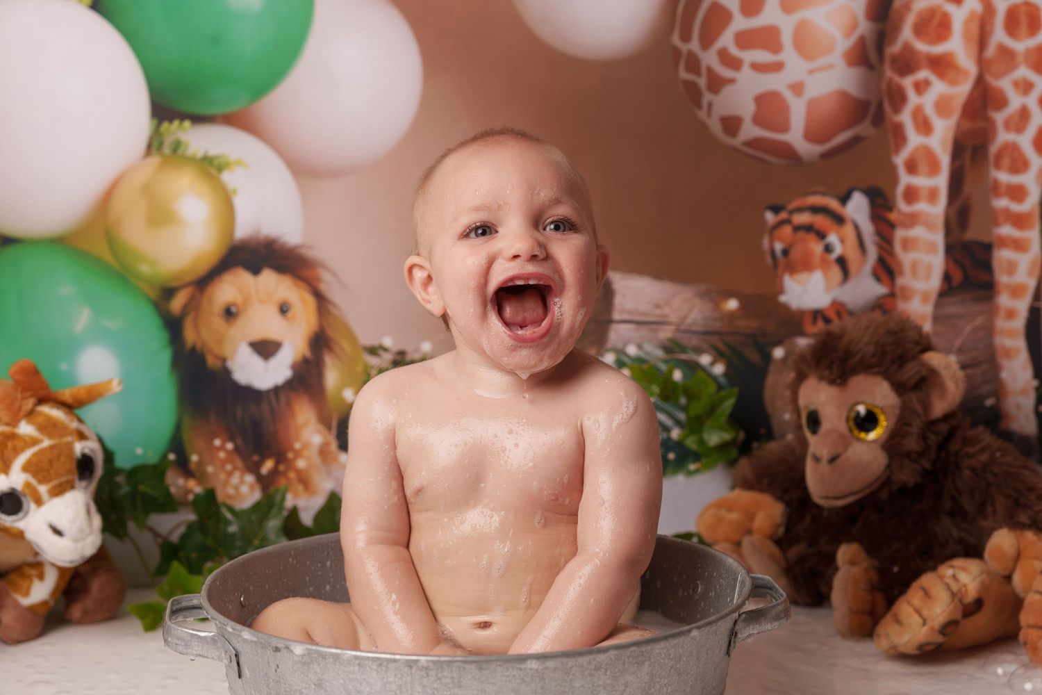 Jungle-themed first birthday photoshoot with stuffed animals and green balloon decorations.