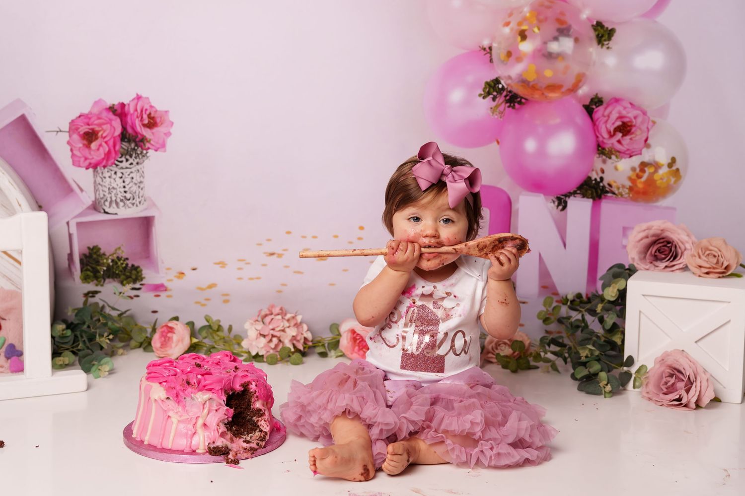 Pink cake smash photography session with decorated cake, tulle skirt and floral balloon arch.