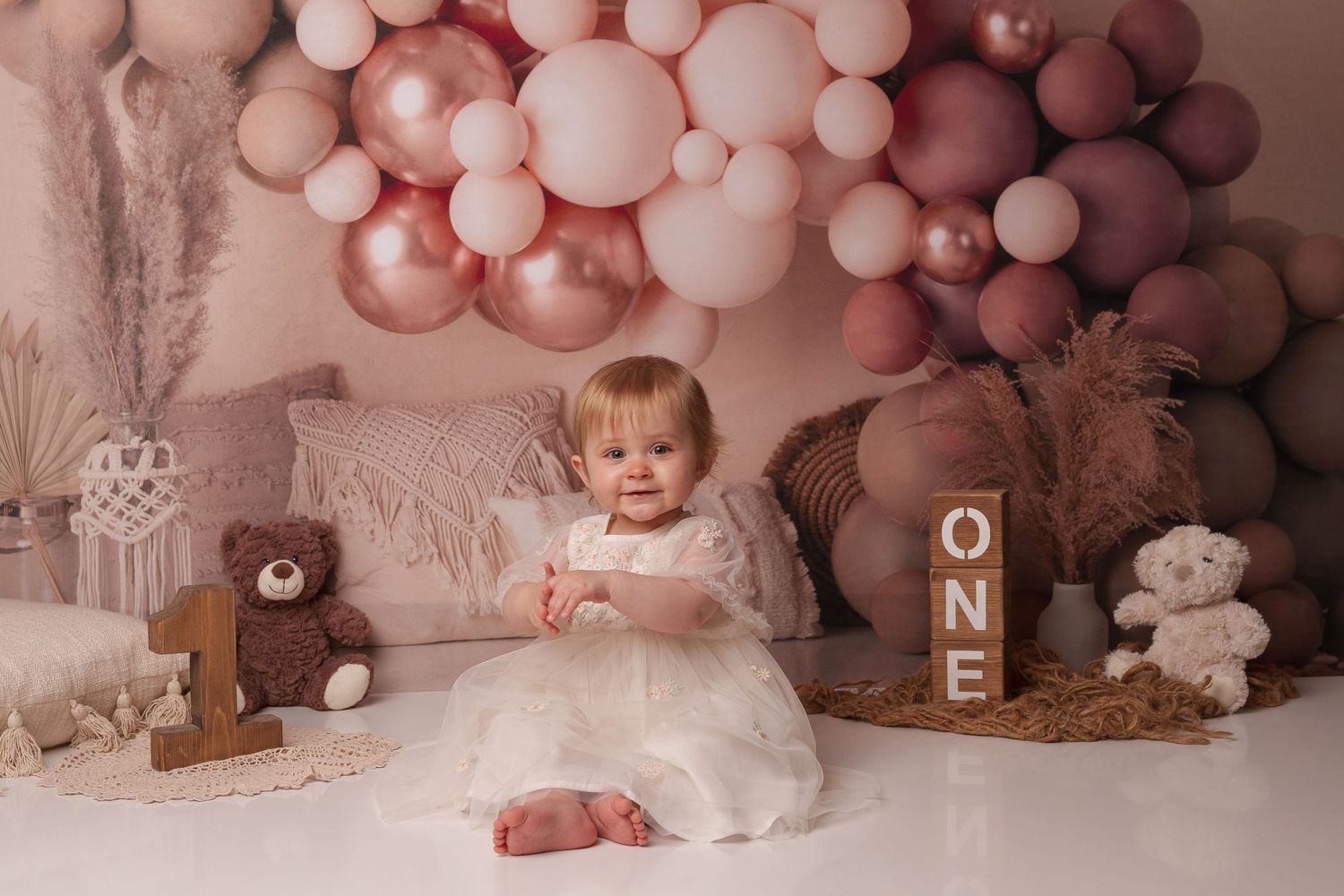 First birthday photo with pink balloon arch and teddy bear decorations.