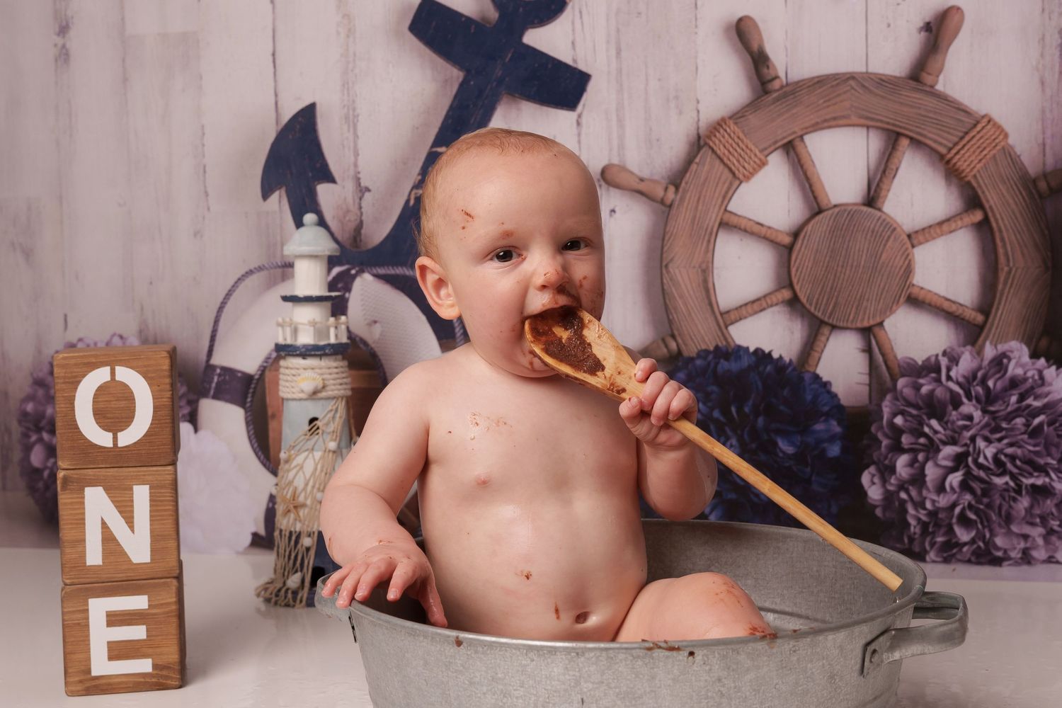 Nautical cake smash photo with baby in metal tub eating cake.