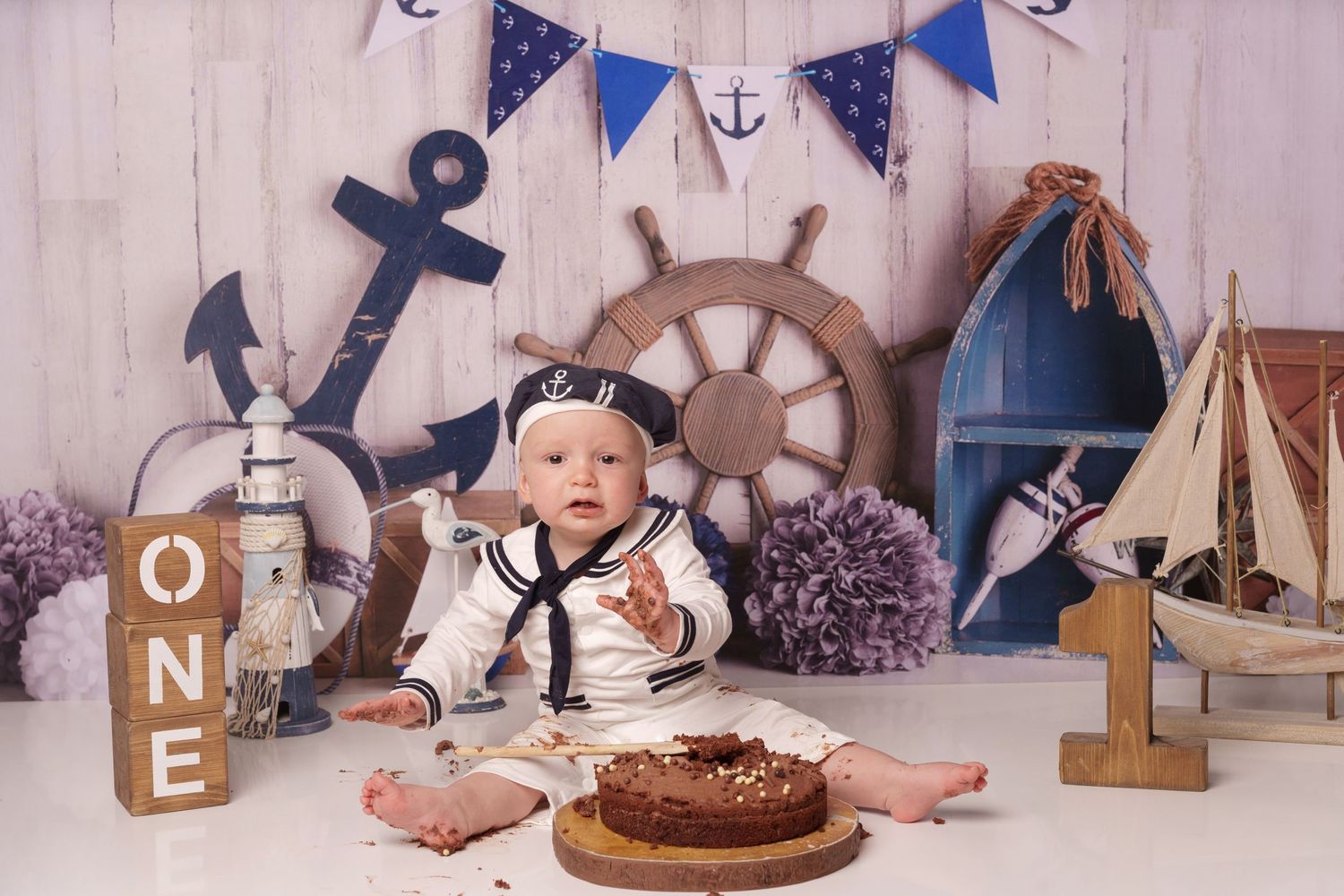 Nautical themed cake smash setup with sailor outfit and wooden wheel prop.