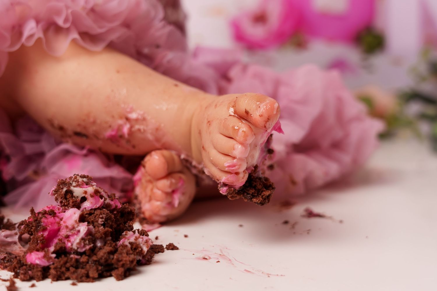 Close-up of tiny feet covered in pink frosting and cake crumbs during cake smash session.