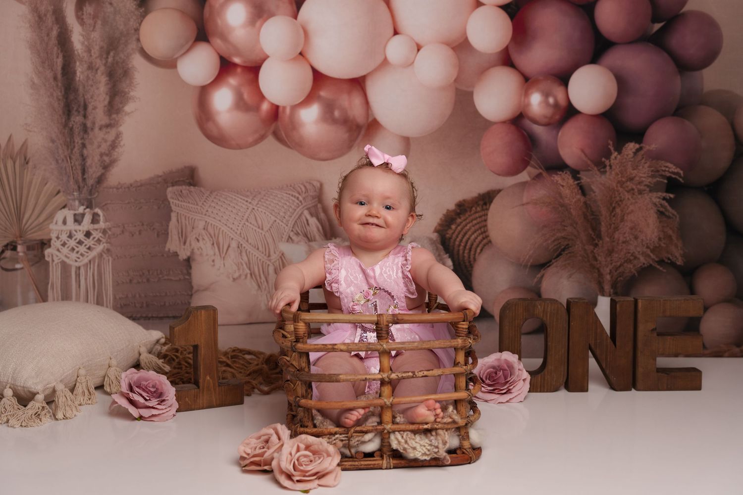 Rustic first birthday setup with pink balloon arch and wooden basket prop.