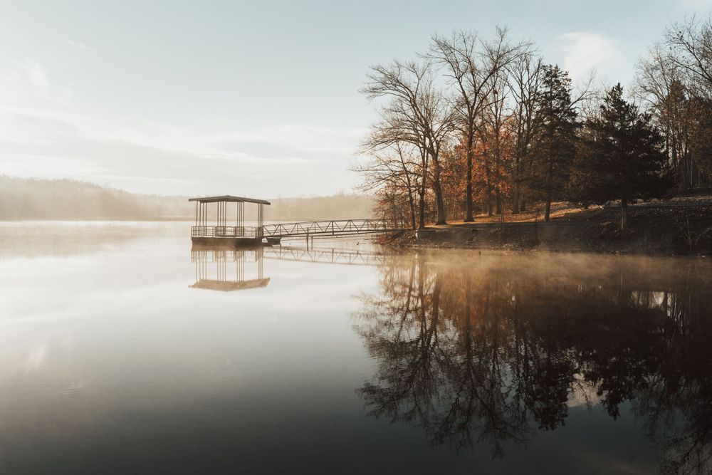 Panoramic view of a tranquil lake with a wooden dock extending into calm waters at sunrise.