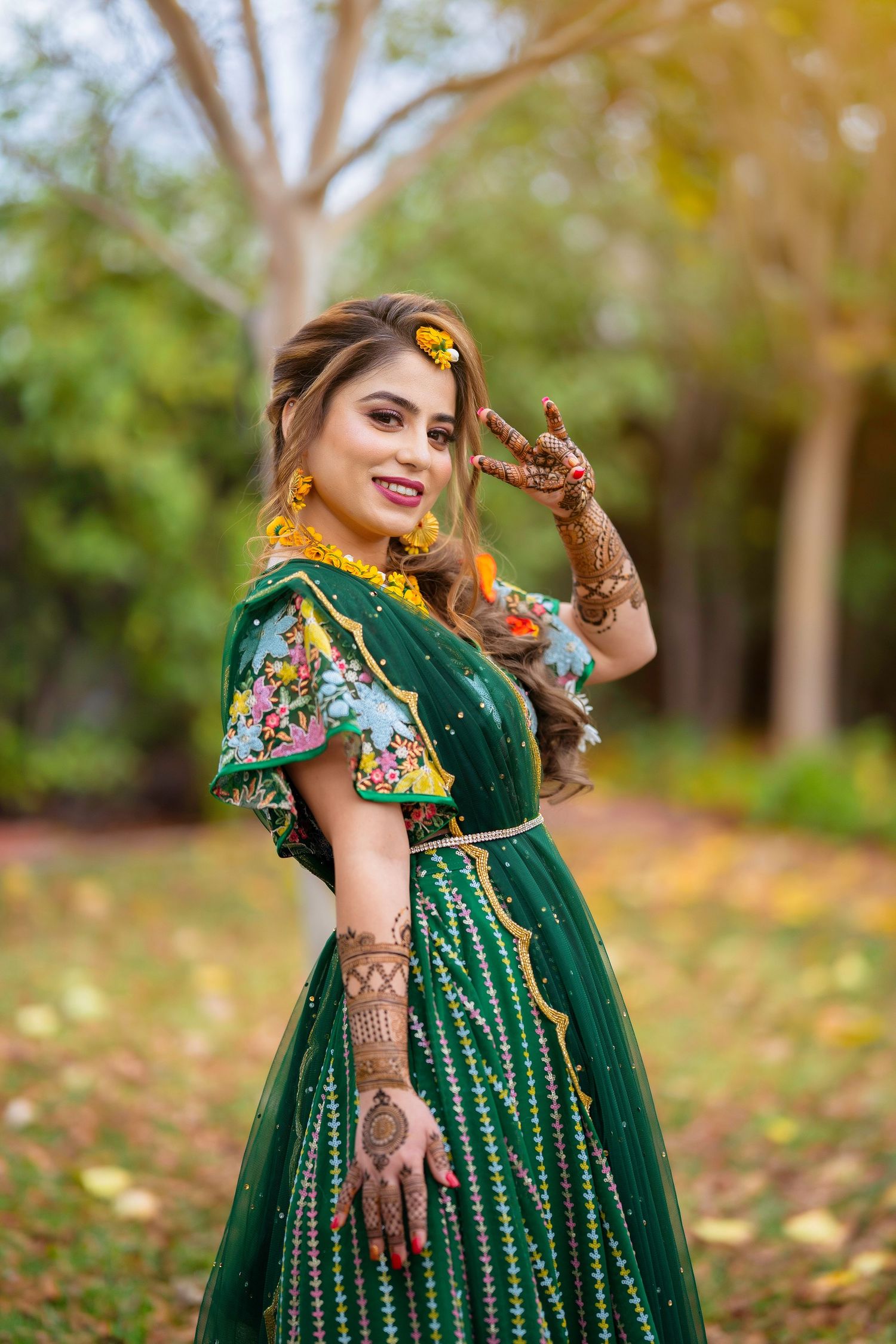 Woman in traditional green floral lehenga shows detailed mehndi designs in outdoor setting.