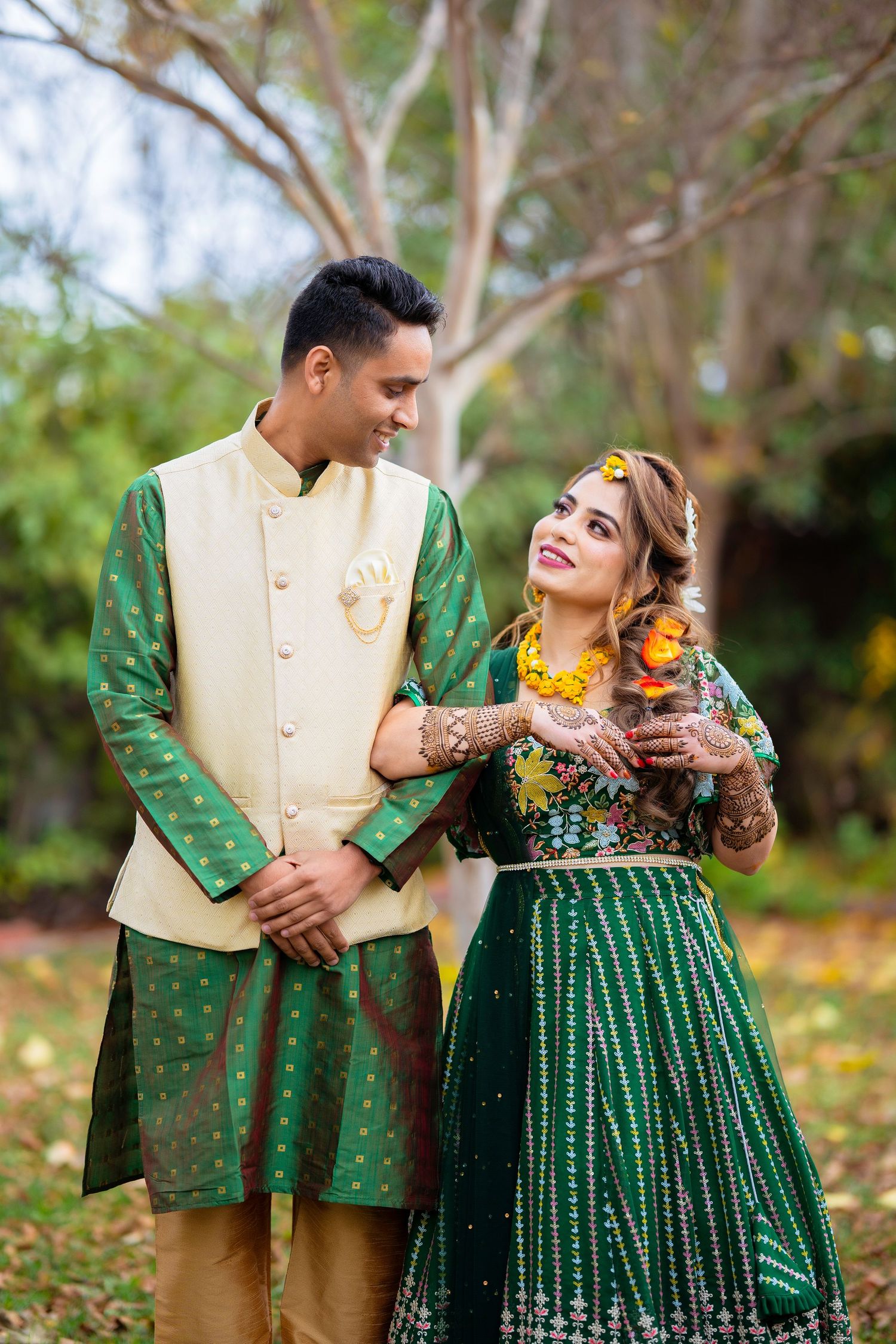 Couple in coordinating green traditional outfits share intimate moment in garden setting.