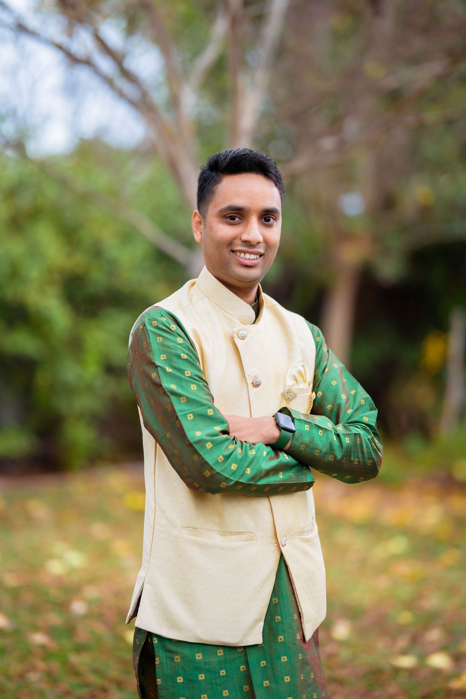 Groom in cream and green sherwani poses confidently in autumn garden.